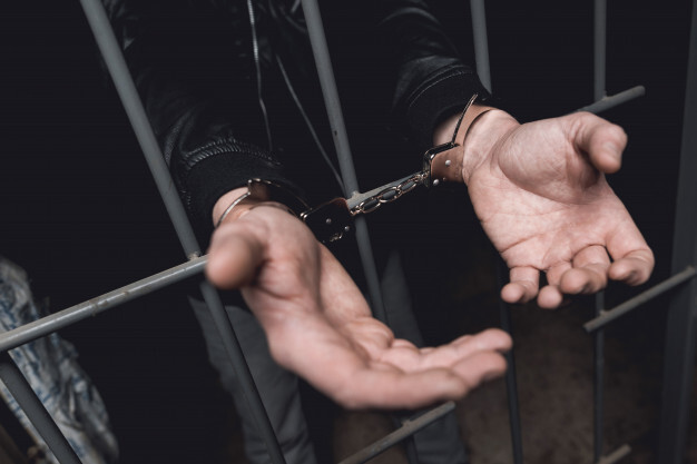 man-in-handcuffs-behind-bars-in-a-police-station_85574-1297