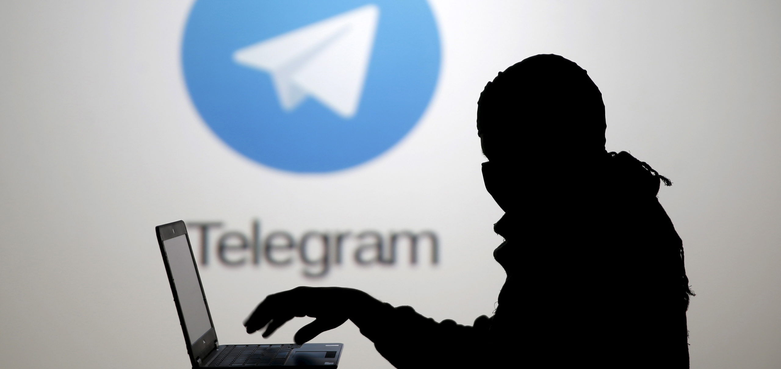 A man poses with a laptop in front of the Telegram logo in this picture illustration taken in Zenica